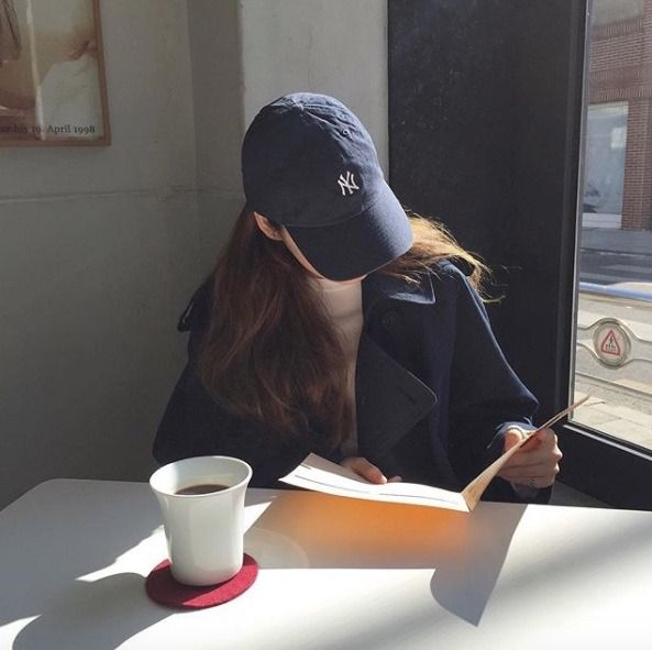 a woman sitting at a table with a book and coffee in front of her looking out the window