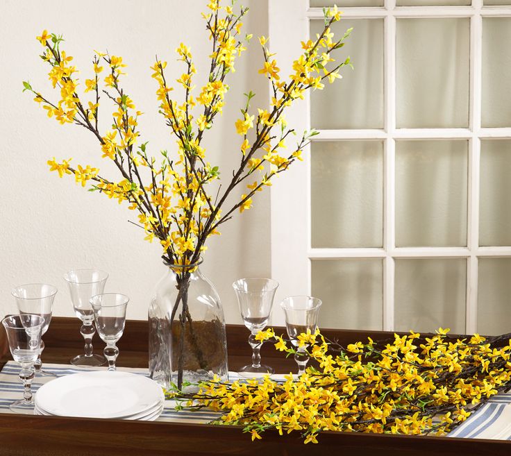 yellow flowers are in vases on a table set with glasses and placemats