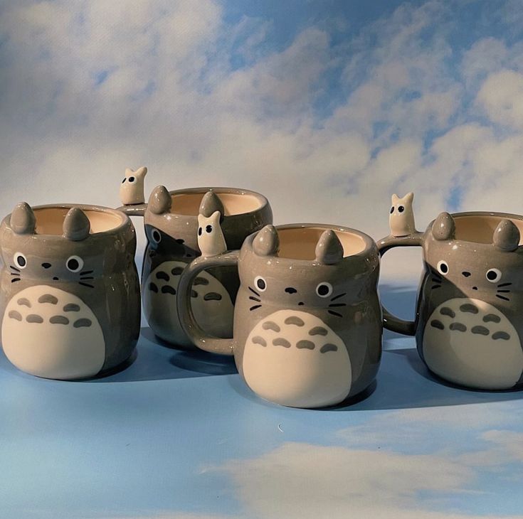 four ceramic mugs with different designs on them sitting in front of a cloudy sky