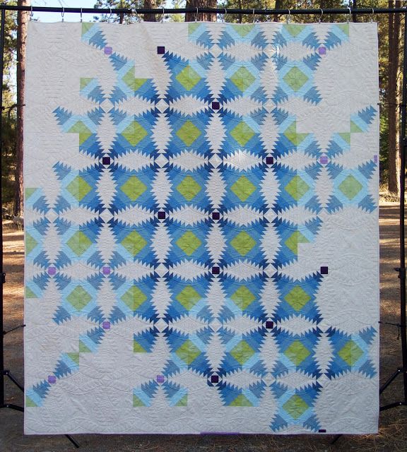 a blue and green quilt is hanging on a metal fence in front of some trees