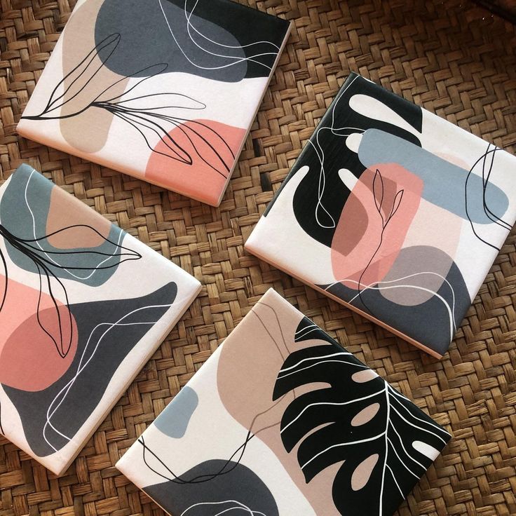 four square coasters with abstract designs on them sitting on a wicker tablecloth