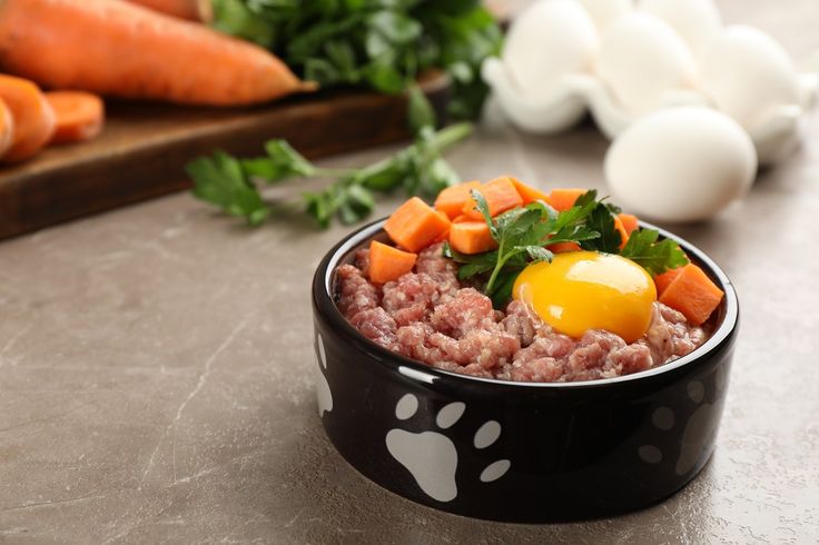 a bowl filled with meat and an egg on top of it next to carrots