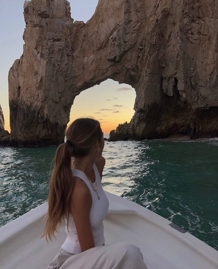 a woman sitting on the back of a boat in front of an arch shaped rock formation