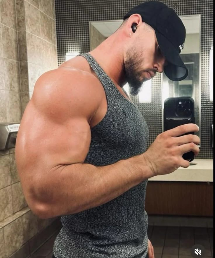 a man taking a selfie in the bathroom with his cell phone and hat on