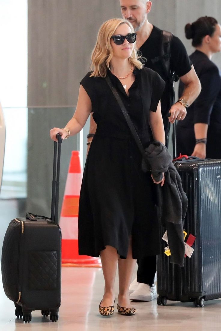 a woman is walking with her luggage at the airport while two other people are behind her