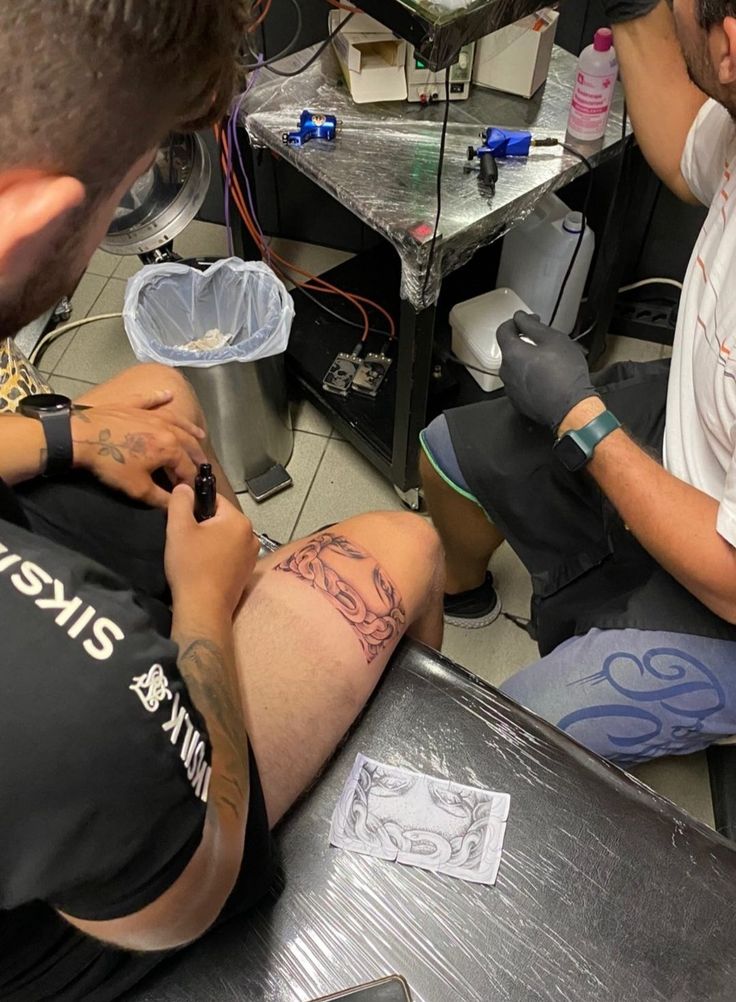 two men sitting in a room with tattoos on their legs