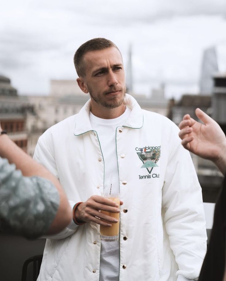 a man wearing a white jacket and holding a drink