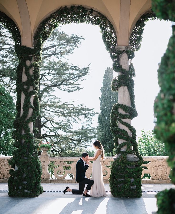 a bride and groom standing in front of an arch covered with greenery at their wedding