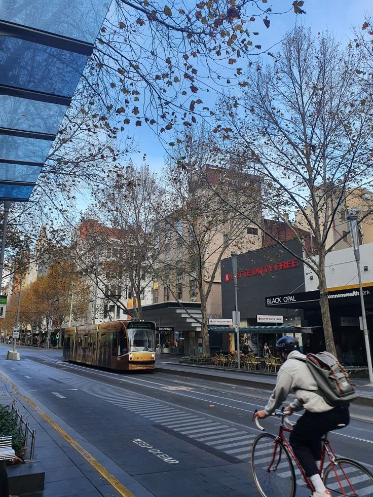 a person riding a bike down the street with a bus in the back ground and buildings on both sides