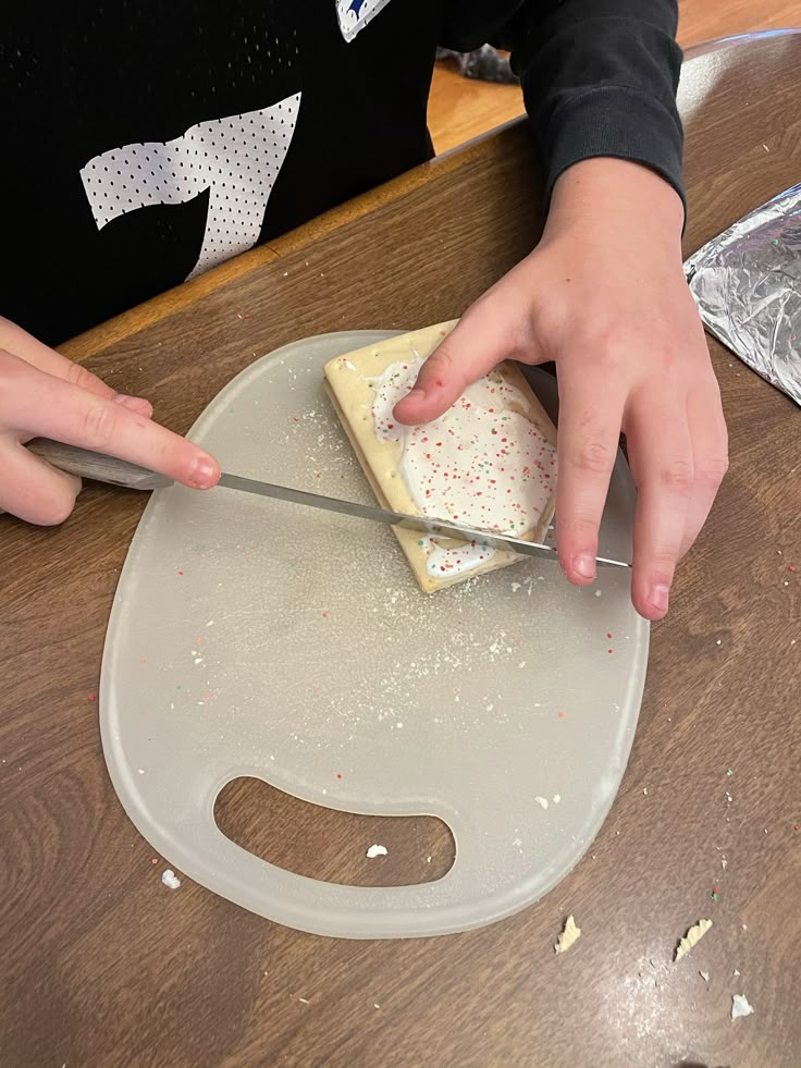 a person cutting into a piece of cake on top of a wooden table with a knife