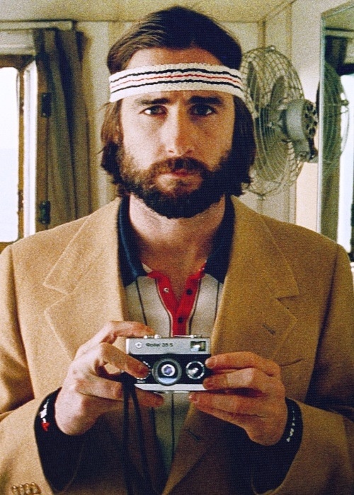 a man holding a camera in front of his face and wearing a head band on top of his head