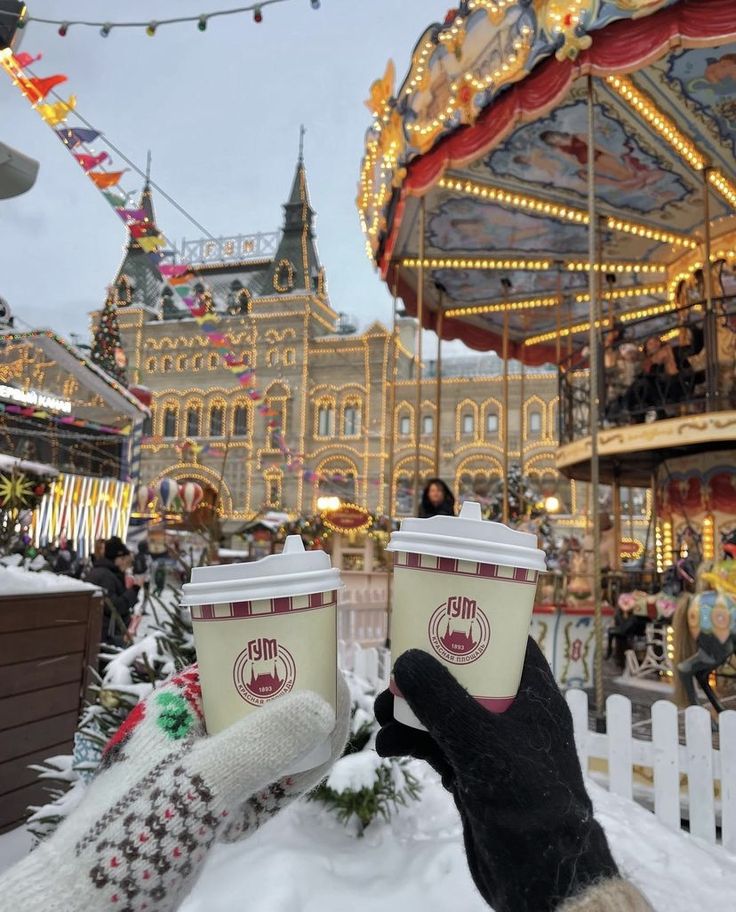 two cups of coffee in the snow near a merry - go - round at an amusement park