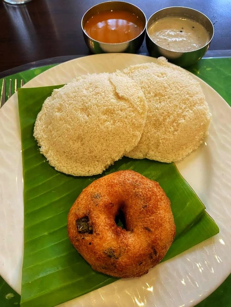 a white plate topped with food on top of a green leaf next to sauces