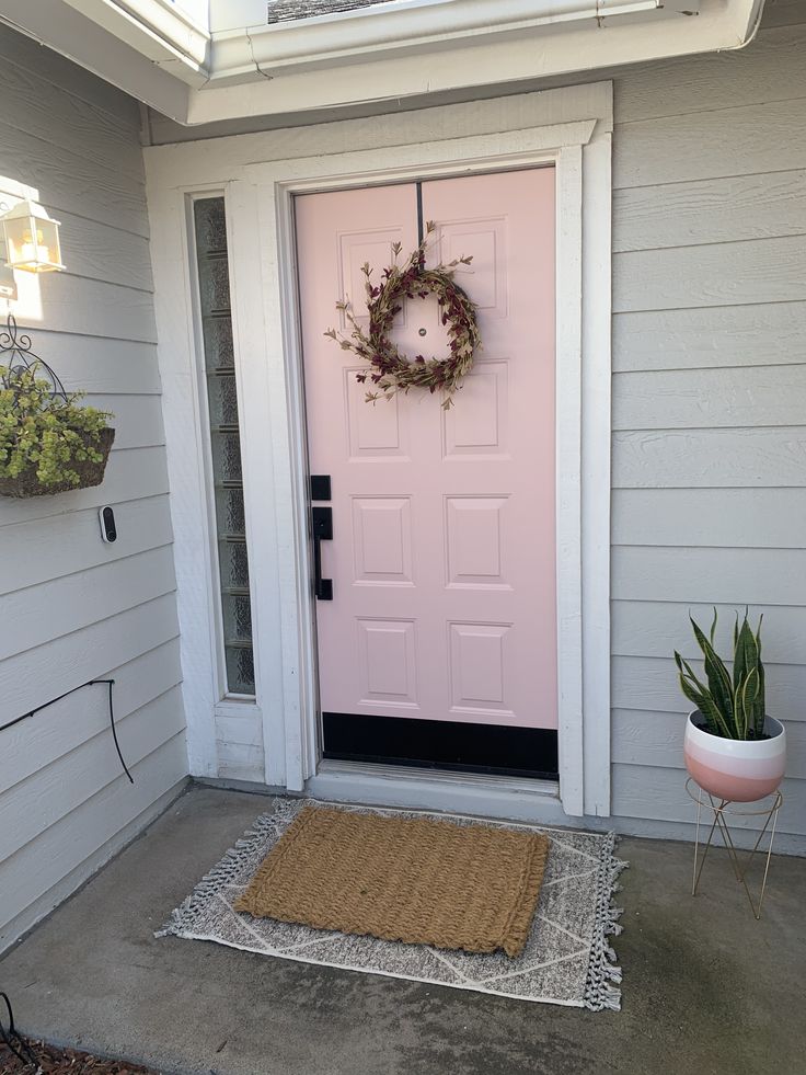 a pink door with a wreath hanging on it's front door and a potted plant next to it