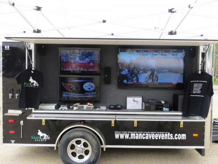 a food truck with two televisions on it's side and some t - shirts hanging from the back