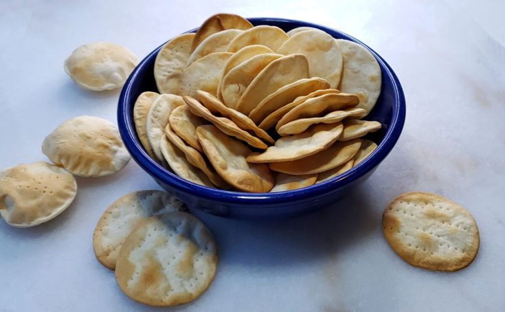 a blue bowl filled with crackers on top of a white counter next to cookies