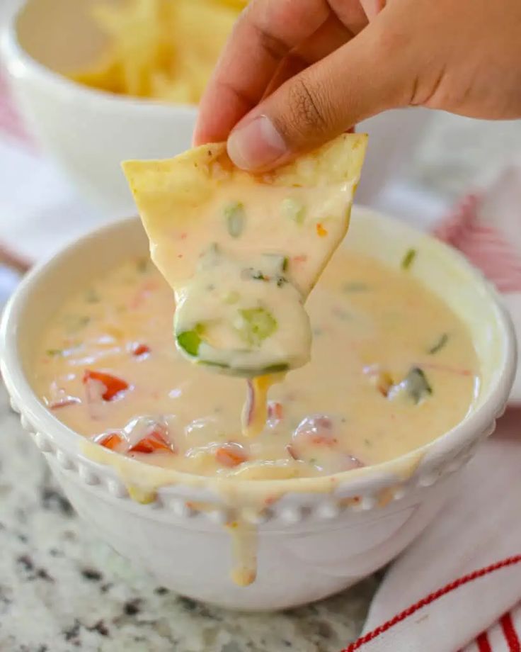 a hand dipping a tortilla chip into a bowl of quesadilla soup