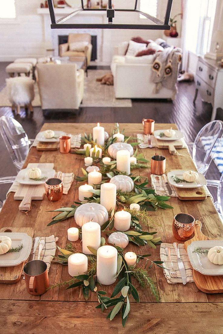 a wooden table topped with lots of white candles and greenery on top of it