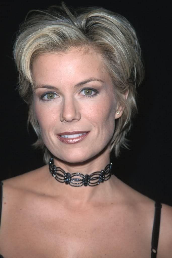 a woman with blonde hair wearing a black choker and smiling at the camera while standing in front of a dark background