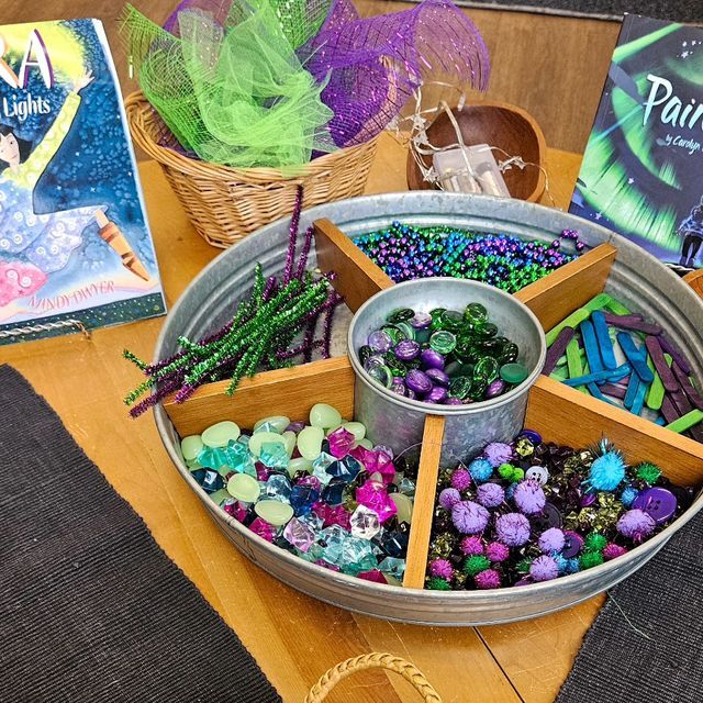 a metal bowl filled with lots of beads next to two books on top of a wooden table