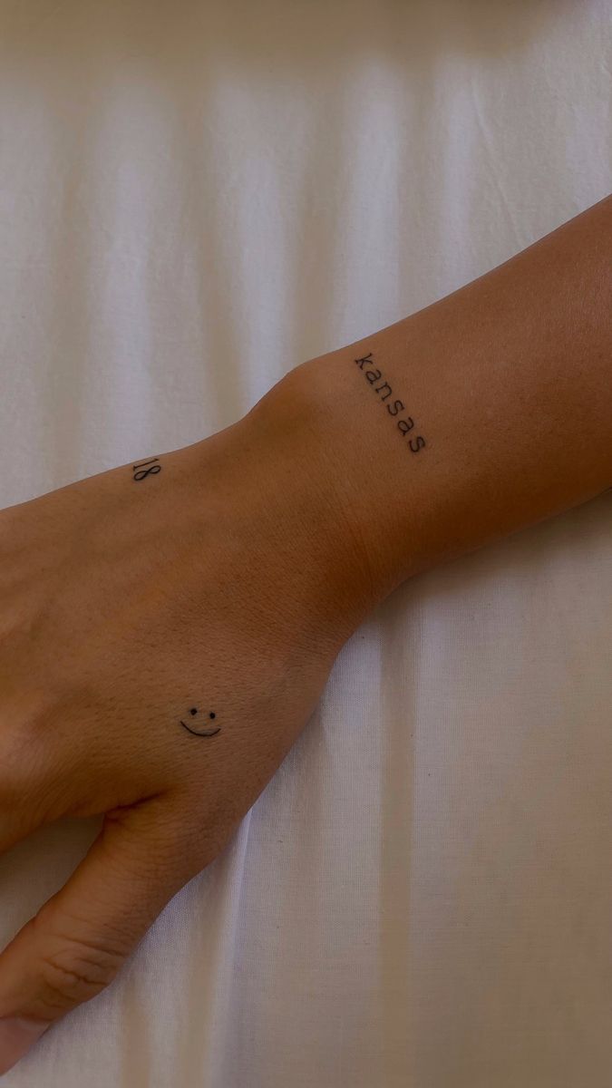 a person's hand with a smiley face tattoo on it and the word happiness written in cursive writing