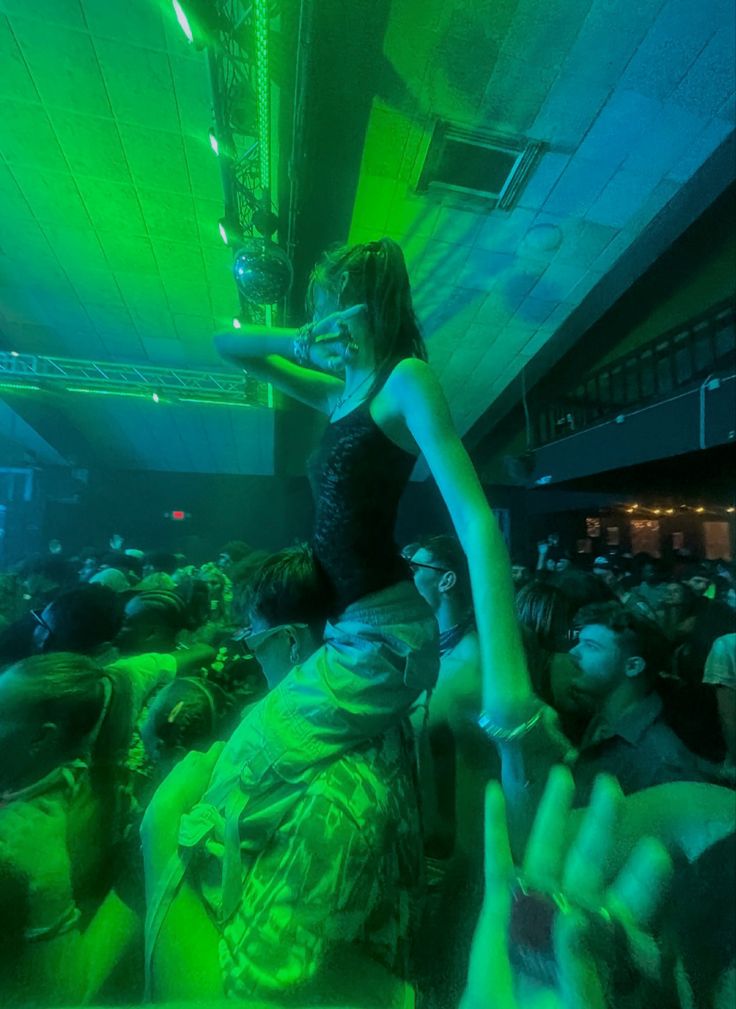 a woman standing on top of a crowd of people in a room with green lighting