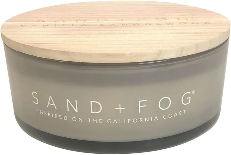 the sand and fog candle is in a glass container with a wooden lid that says, inspired on the california coast