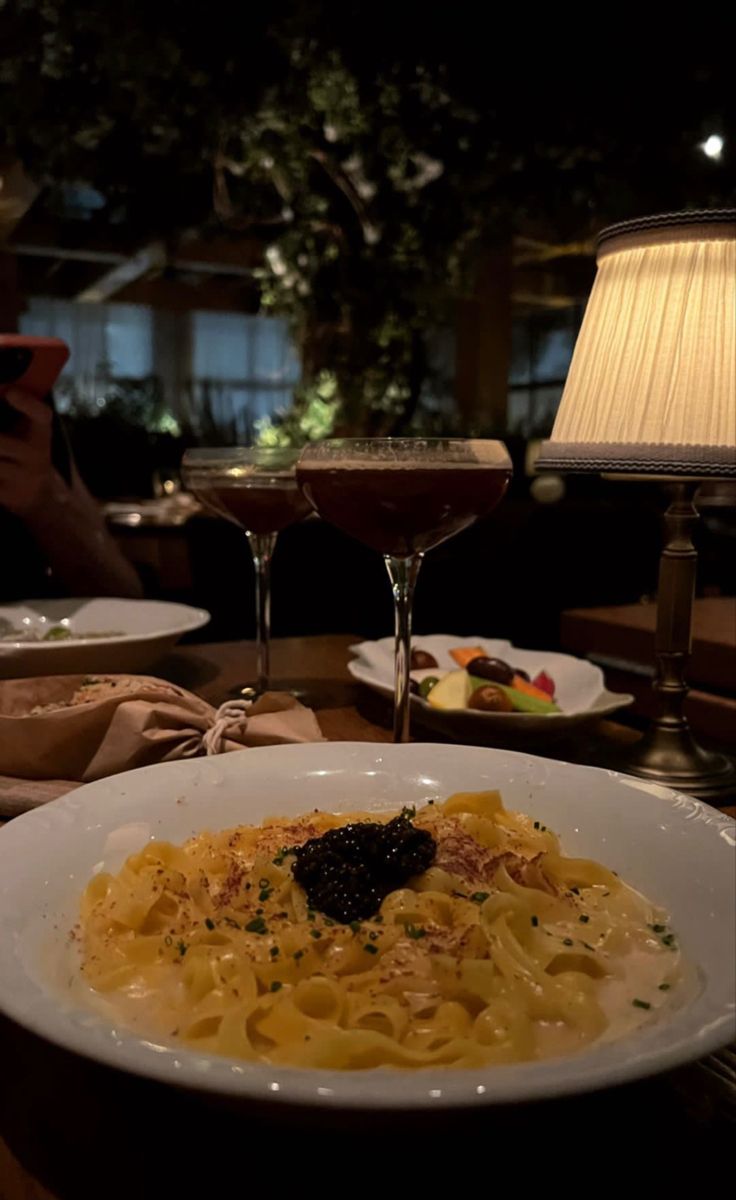 a plate of pasta on a table with two glasses of wine in front of it