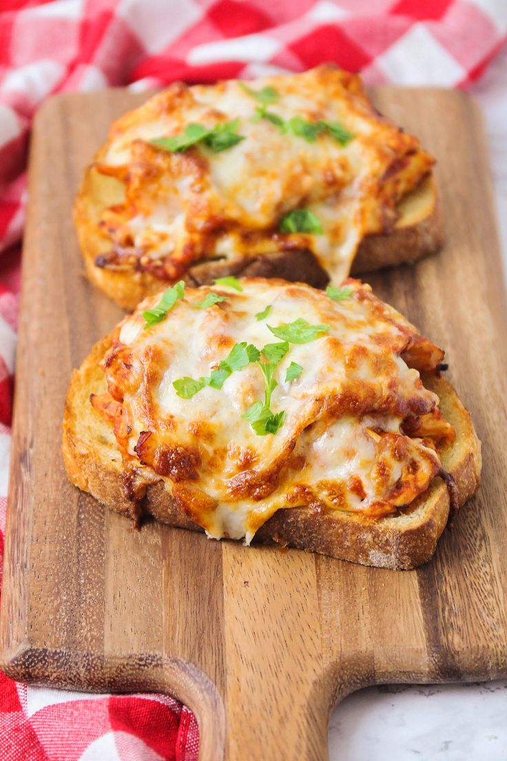 two cheesy pizzas sitting on top of a wooden cutting board