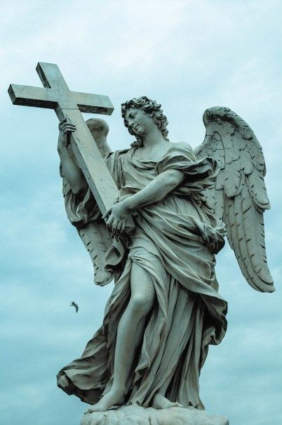 an angel holding a cross on top of a statue