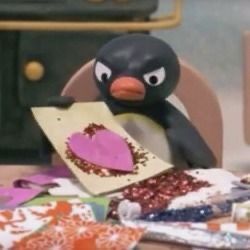 a penguin sitting on top of a wooden table next to a piece of paper with a heart