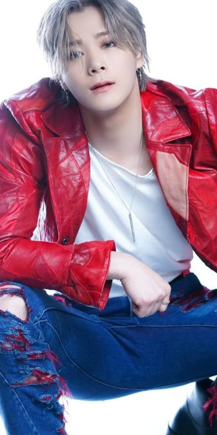 a person sitting on the ground wearing a red leather jacket and ripped blue jeans with one leg up