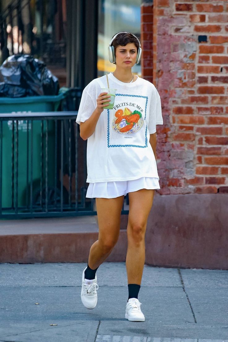 a woman walking down the street with headphones in her ears and holding a drink