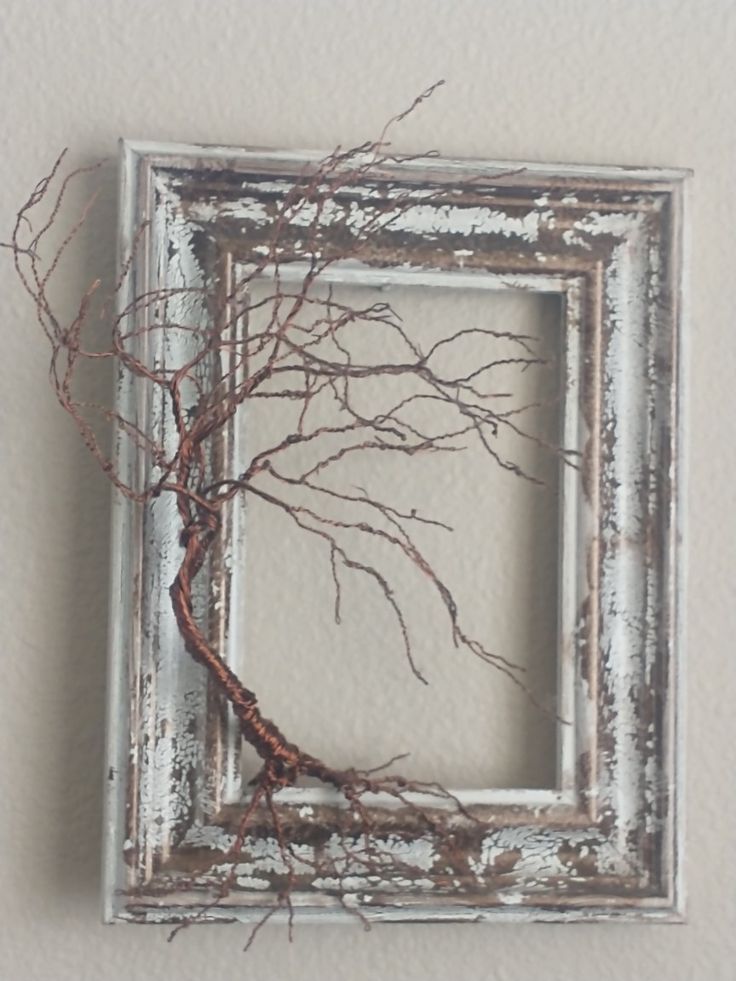 an old frame with branches in it hanging on the wall next to a white wall