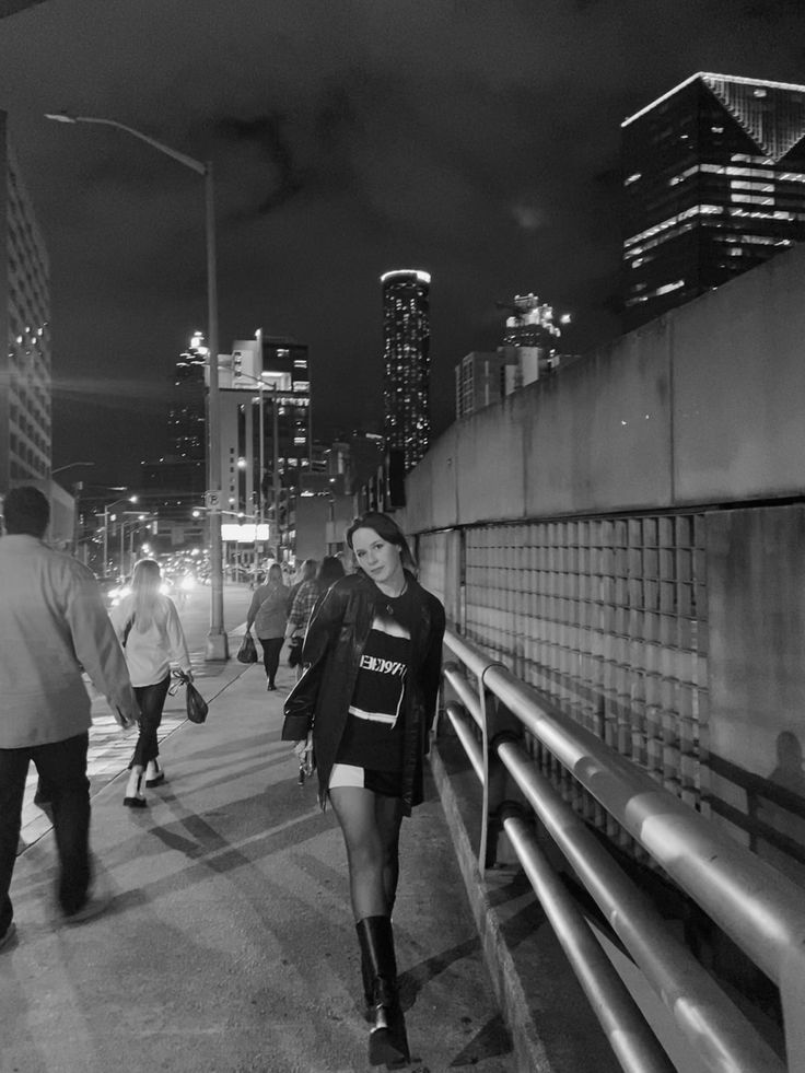 black and white photograph of people walking on the sidewalk at night with skyscrapers in the background