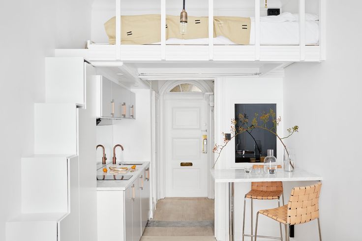 a kitchen with white walls and flooring next to a staircase leading up to a loft bed