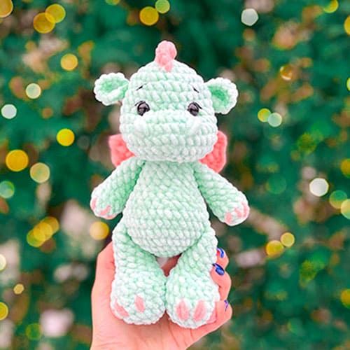 a hand holding a small crocheted stuffed animal in front of a tree with lights