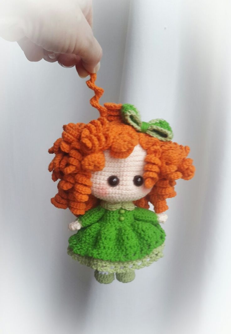 a hand is holding a small doll with red hair and green dress on it's head