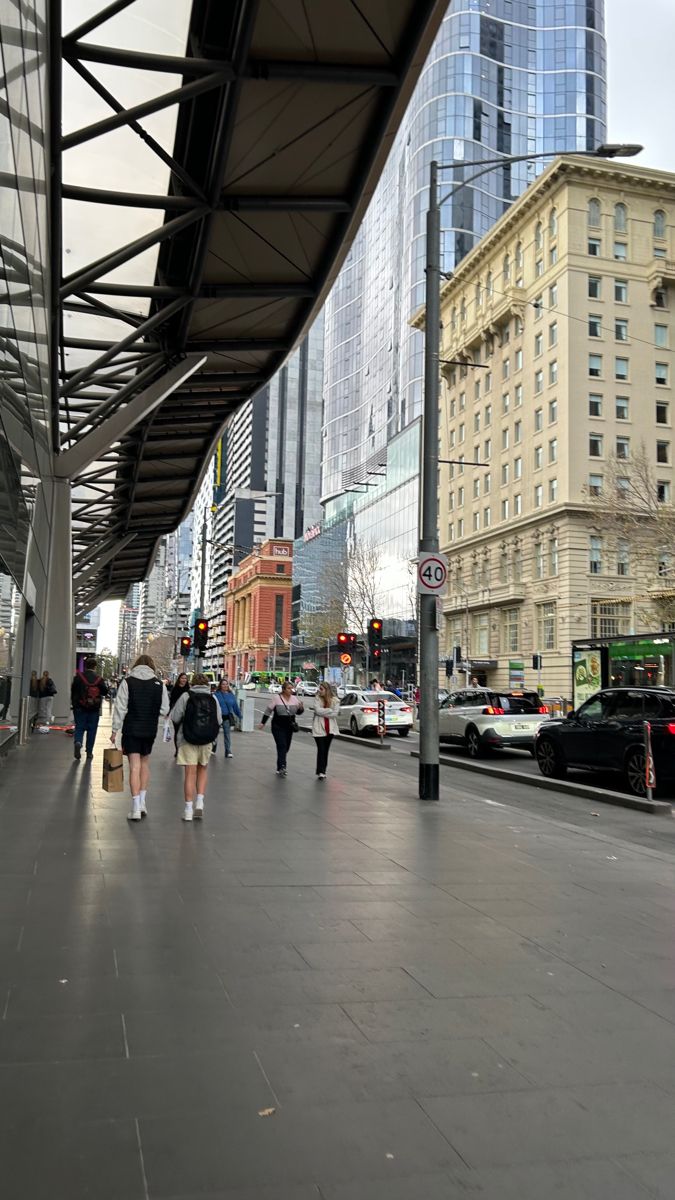 people are walking down the sidewalk in front of tall buildings and skyscrapers on a cloudy day