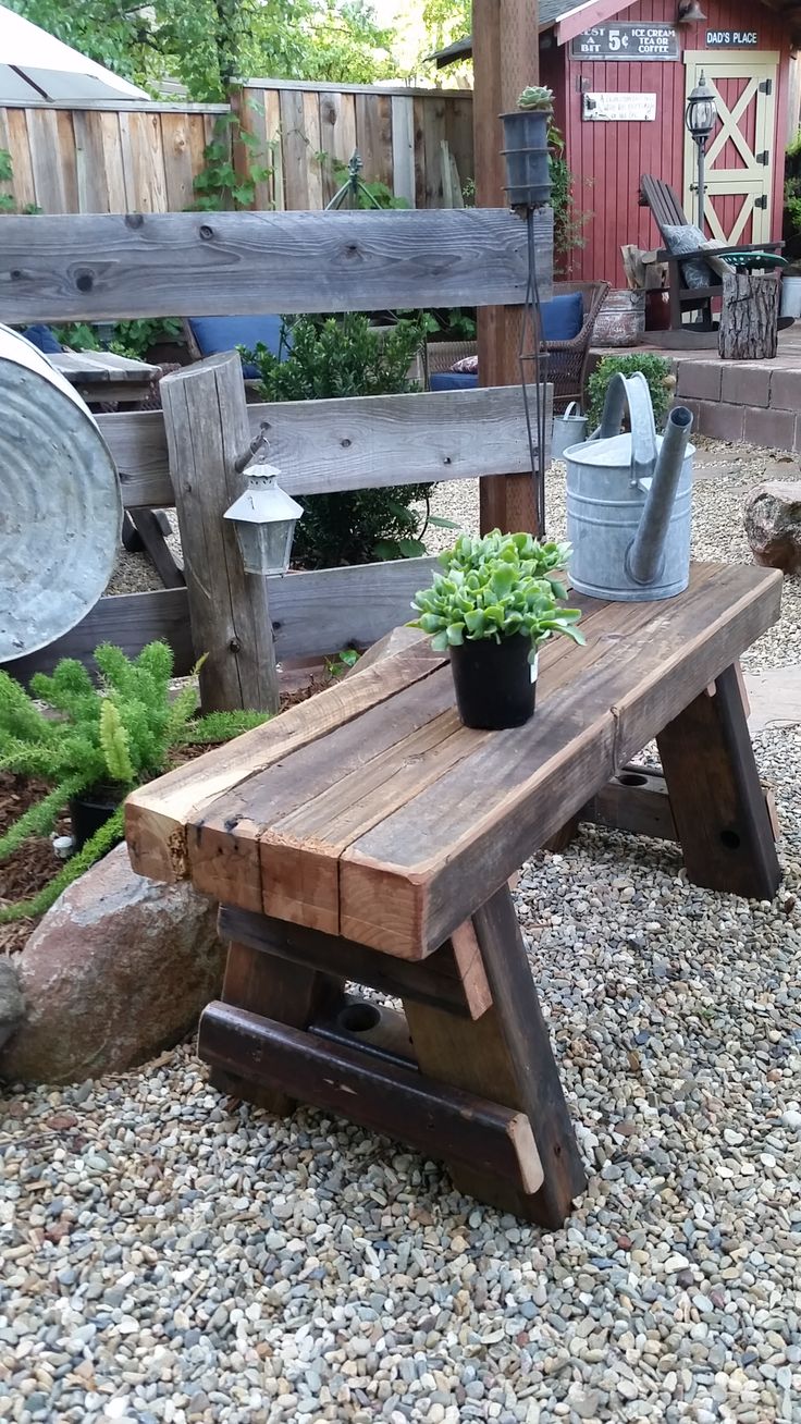 a wooden bench sitting on top of a gravel covered ground next to a potted plant