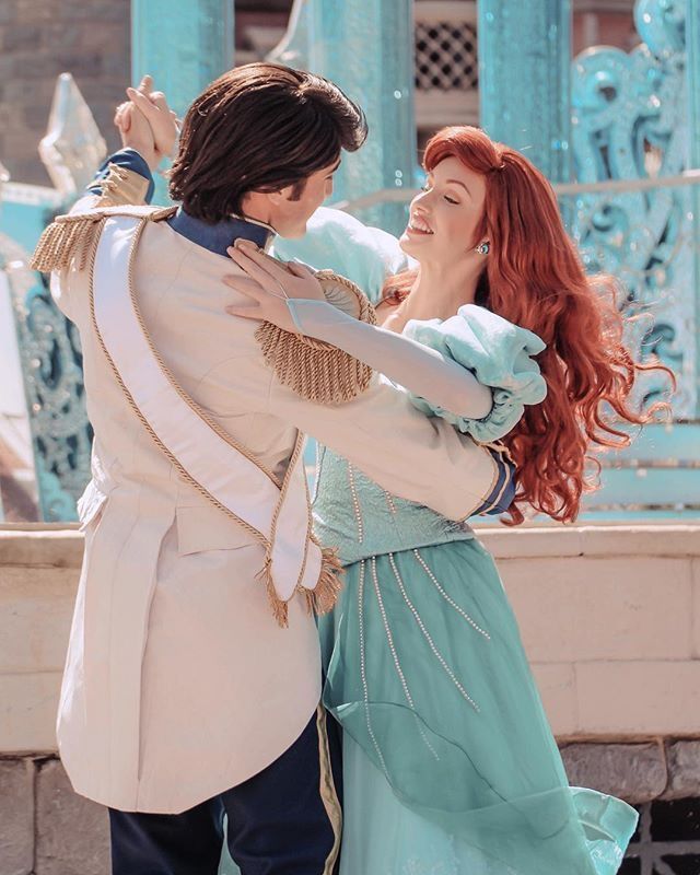 a man and woman dressed as disney characters hugging each other in front of a fountain