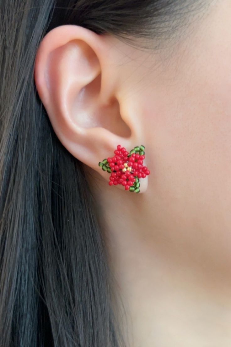 a close up of a person's ear with red flowers on it and green leaves