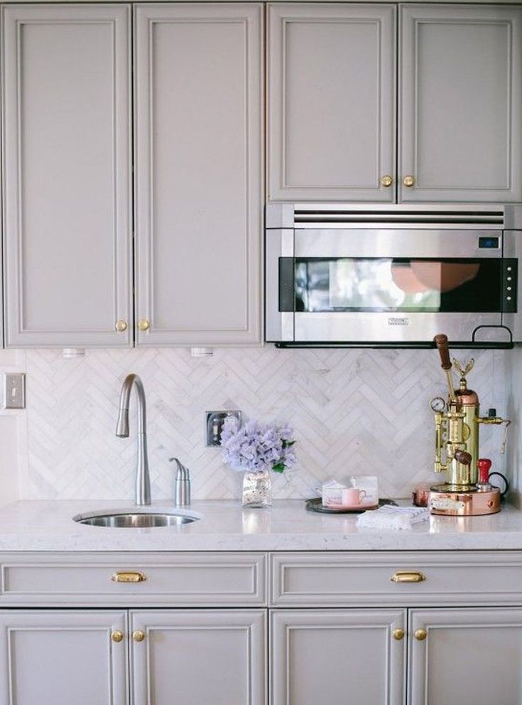 a kitchen with white cabinets and gold hardware on the countertop, along with a silver microwave oven