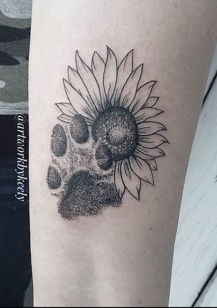 a black and white photo of a paw print with a sunflower tattoo on the arm