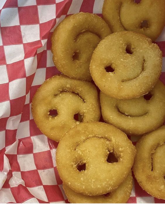 some fried doughnuts are sitting on a checkered tablecloth with a smiley face drawn on them