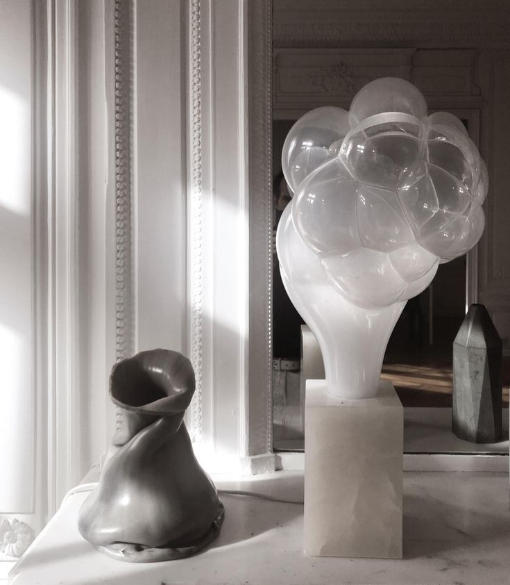 an assortment of vases and sculptures sit on a table in front of a mirror