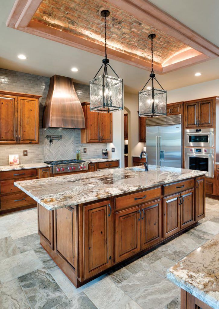 a large kitchen with marble counter tops and wooden cabinets, along with two pendant lights hanging from the ceiling