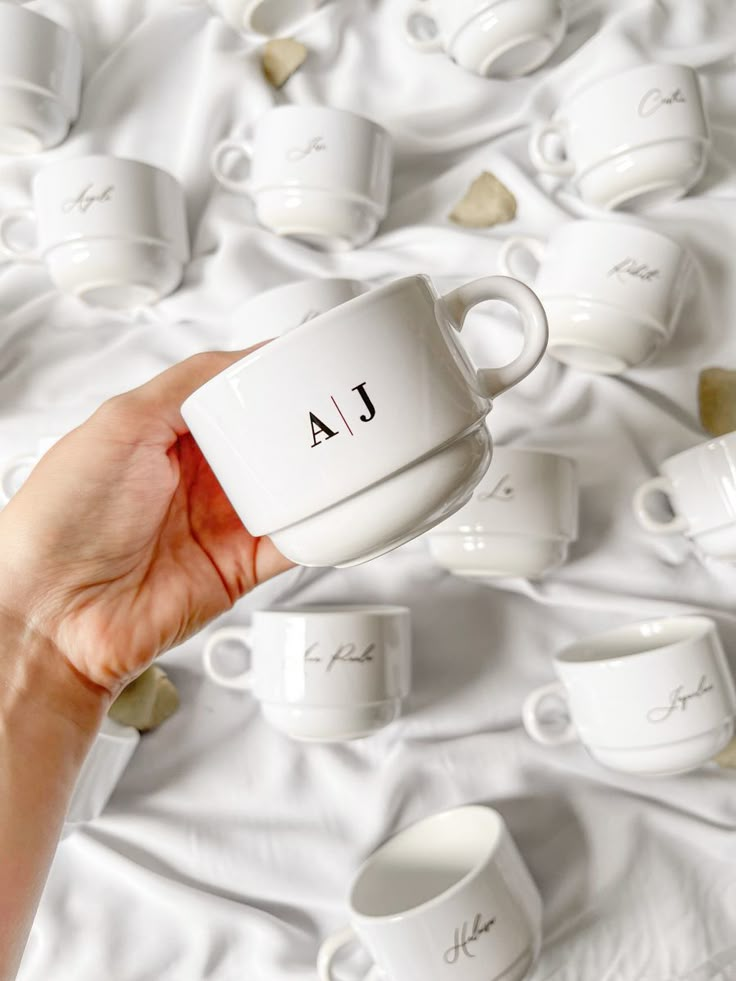 a person holding a coffee cup in front of many cups on a white bed spread