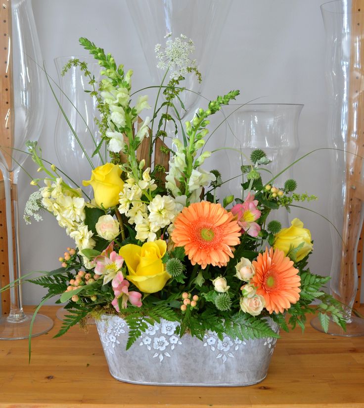 a vase filled with lots of colorful flowers on top of a wooden table next to wine glasses