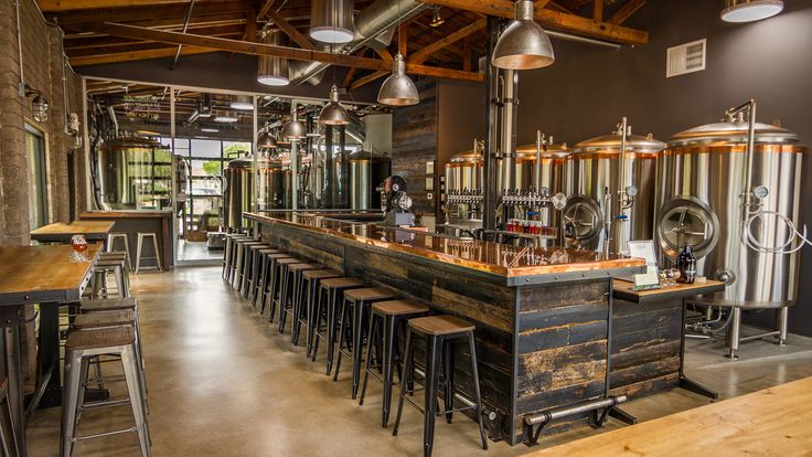 an industrial style bar with lots of stools and beer kegs in the background